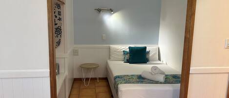 A small, neatly arranged bedroom with a bed, a small stool, and a nightstand.