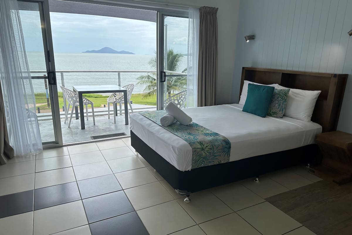 A hotel room with a bed, a view of the sea, and a balcony with a table and chairs.