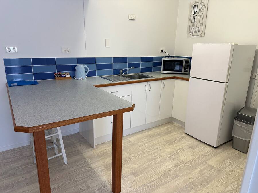 A compact kitchen with a granite countertop, white cabinets, a microwave, and a refrigerator.