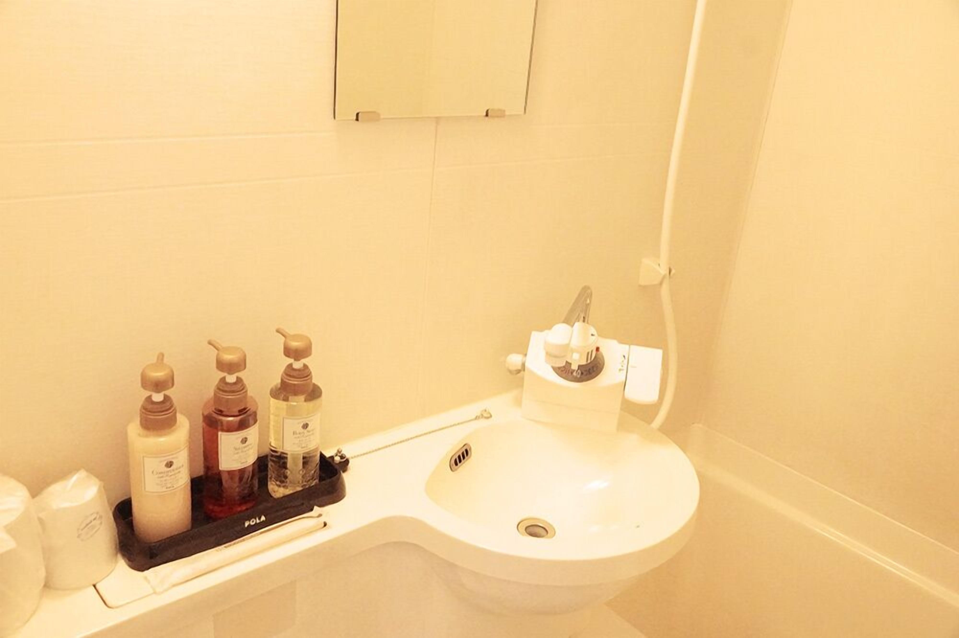A bathroom with a white sink, a mirror, and three bottles of toiletries on a tray.