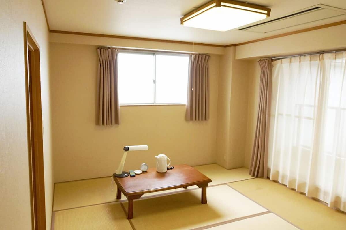 Een traditionele Japanse kamer met tatami vloerbedekking, een lage houten tafel met waterkoker en theepot, en twee ramen met gordijnen.