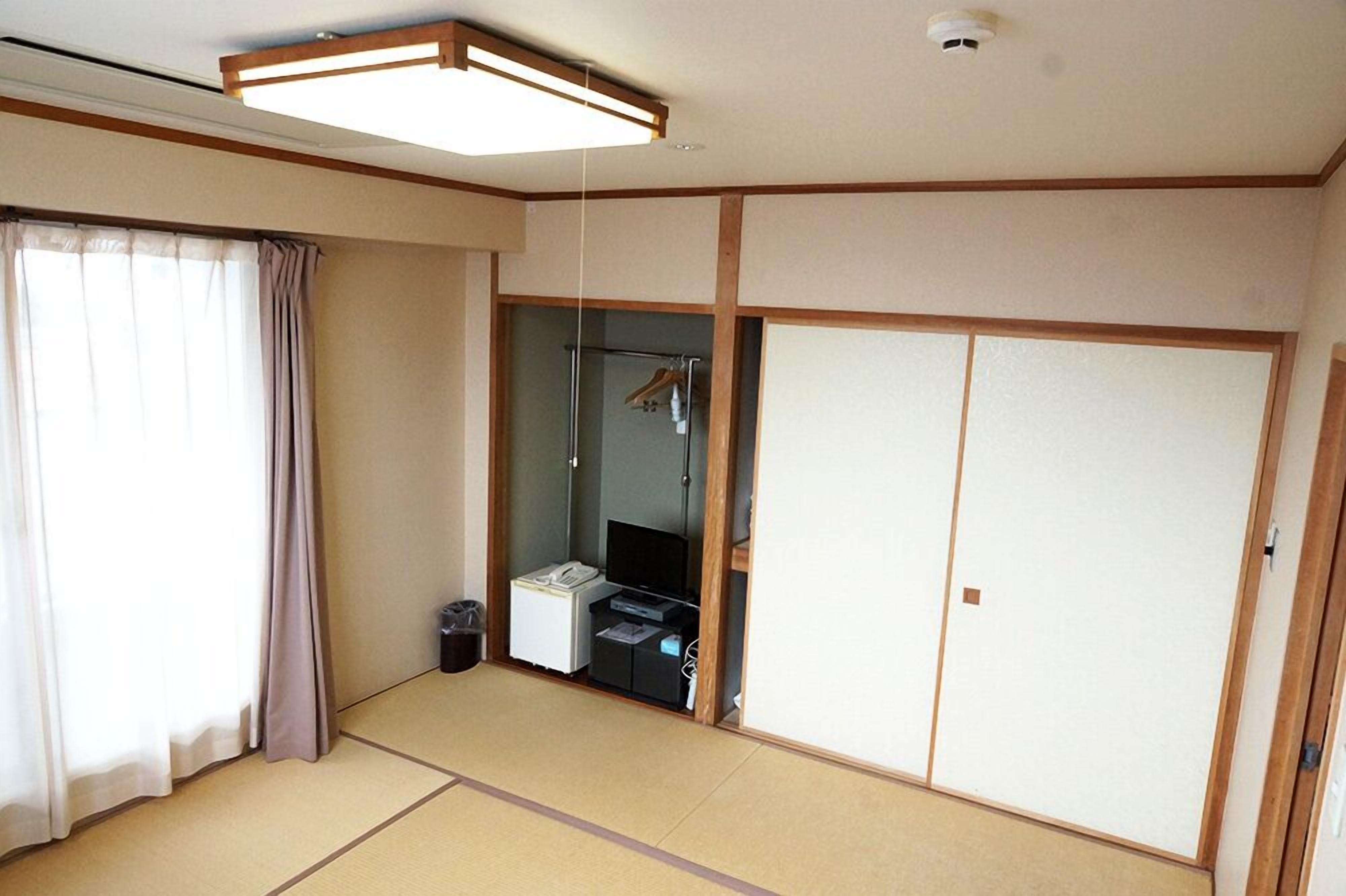 A room with tatami flooring, a sliding door closet, a small desk with a telephone, and a mirror with a hanging robe.