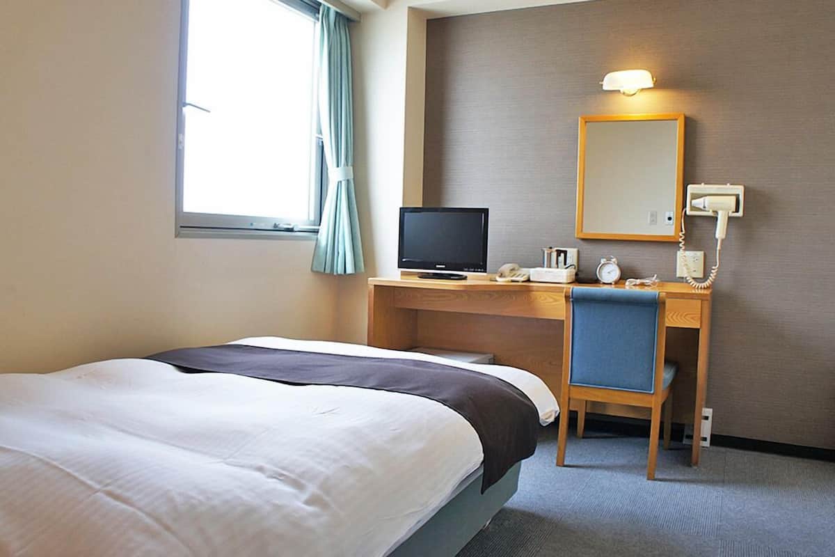 Een hotelkamer met een bed, een bureau met een computer, een telefoon en een spiegel.