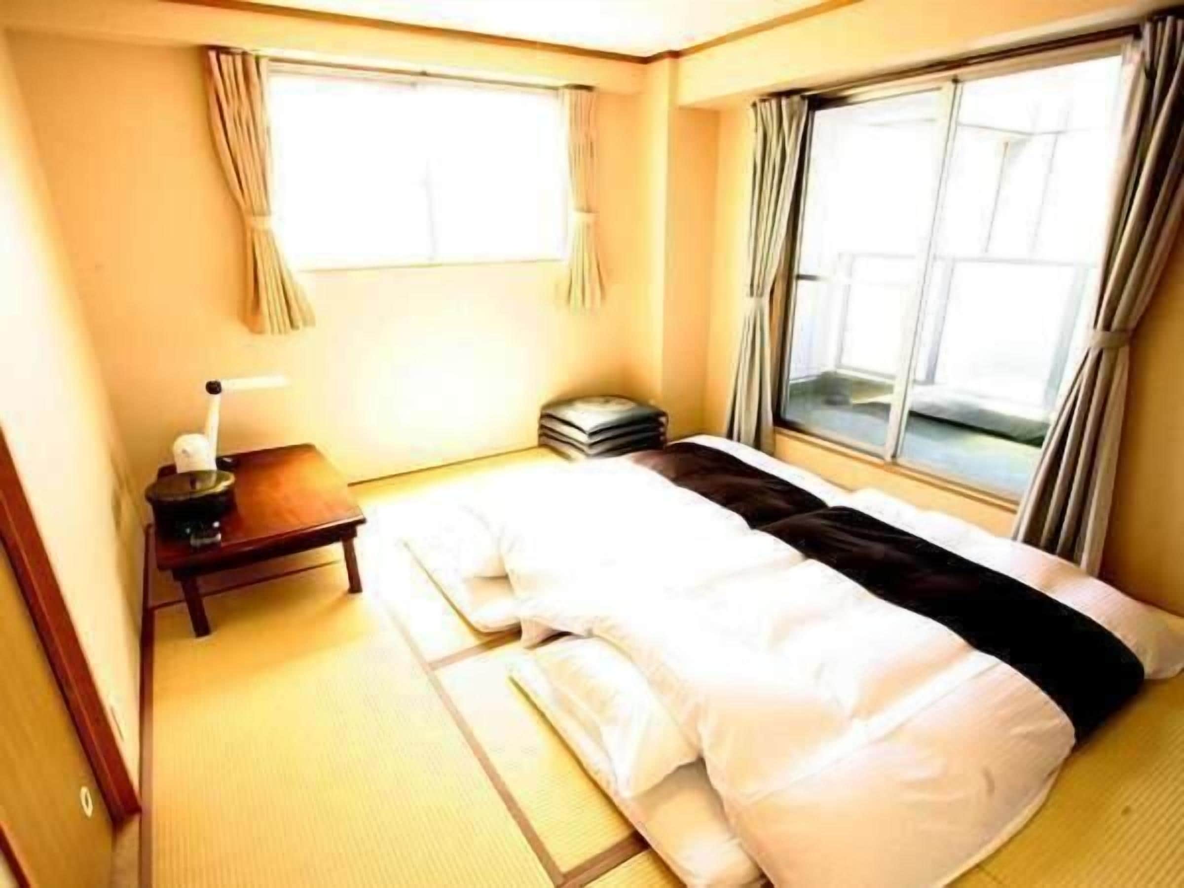 A hotel room with a bed, a nightstand, a lamp, and a window with curtains.