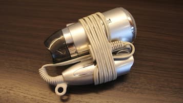 Un altoparlante portatile argentato con un cavo a spirale e una piccola base circolare, appoggiato su una superficie di legno.