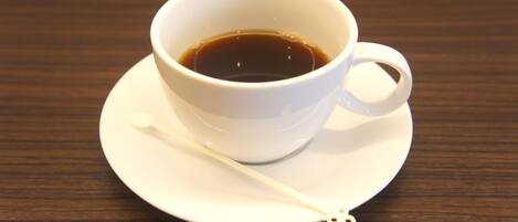 A white cup of coffee on a saucer with a spoon on a wooden table.