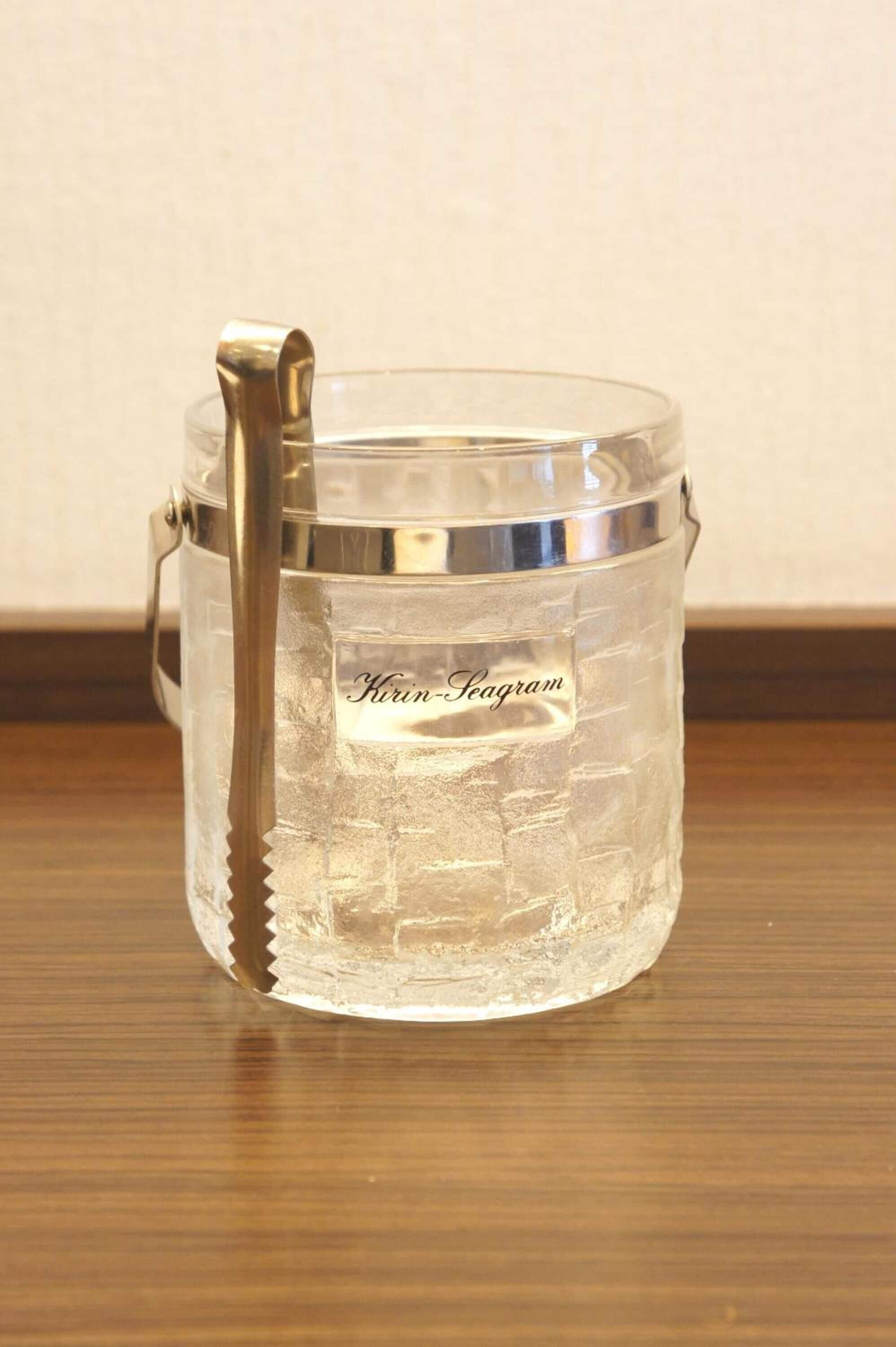 A clear glass ice bucket with a metal handle and a label that reads "Kirin Seagram."