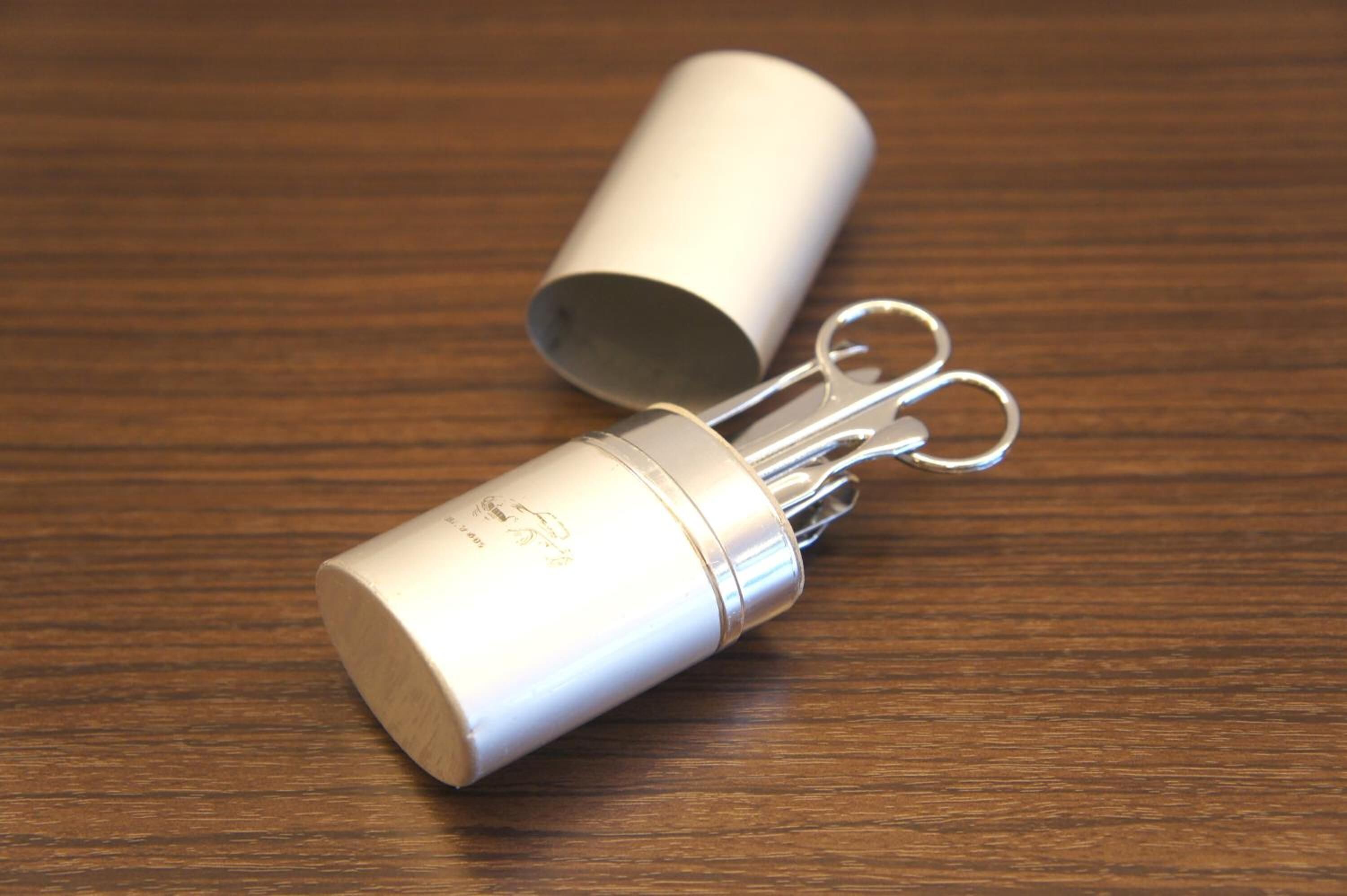 A cylindrical container with a metal clasp and a key ring attached, placed on a wooden surface.