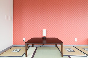 A room with a wooden table, two tatami mats, a red patterned wall, and a white switchboard. - 81's Inn Nakasu - Hostel (Fukuoka)