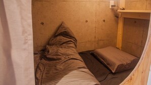 A small, compact room with a single bed, a wooden bench, and a wall-mounted shelf. - Picnic Hostel Osaka (Osaka)