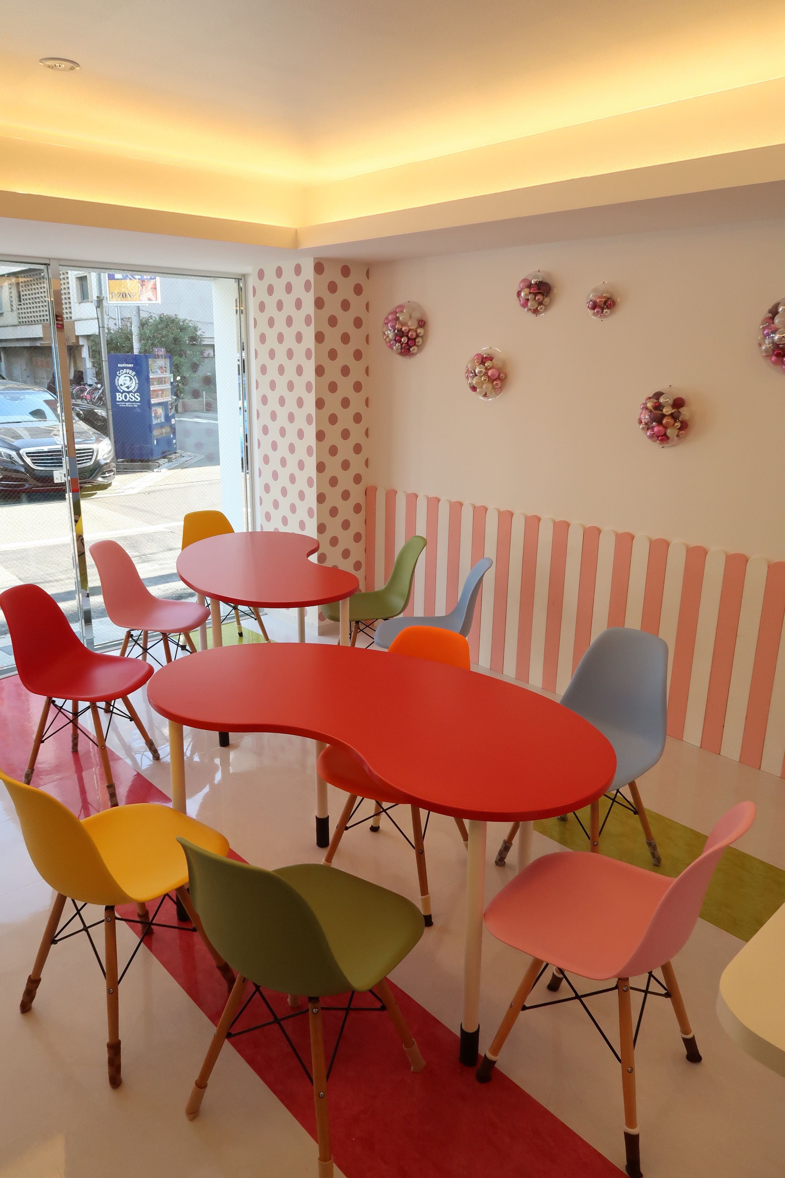 A room with a red table and colorful chairs, a striped wall, and a glass door leading outside.