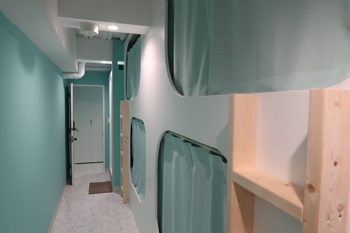 A corridor with teal walls, wooden bunk beds, and a door at the end.