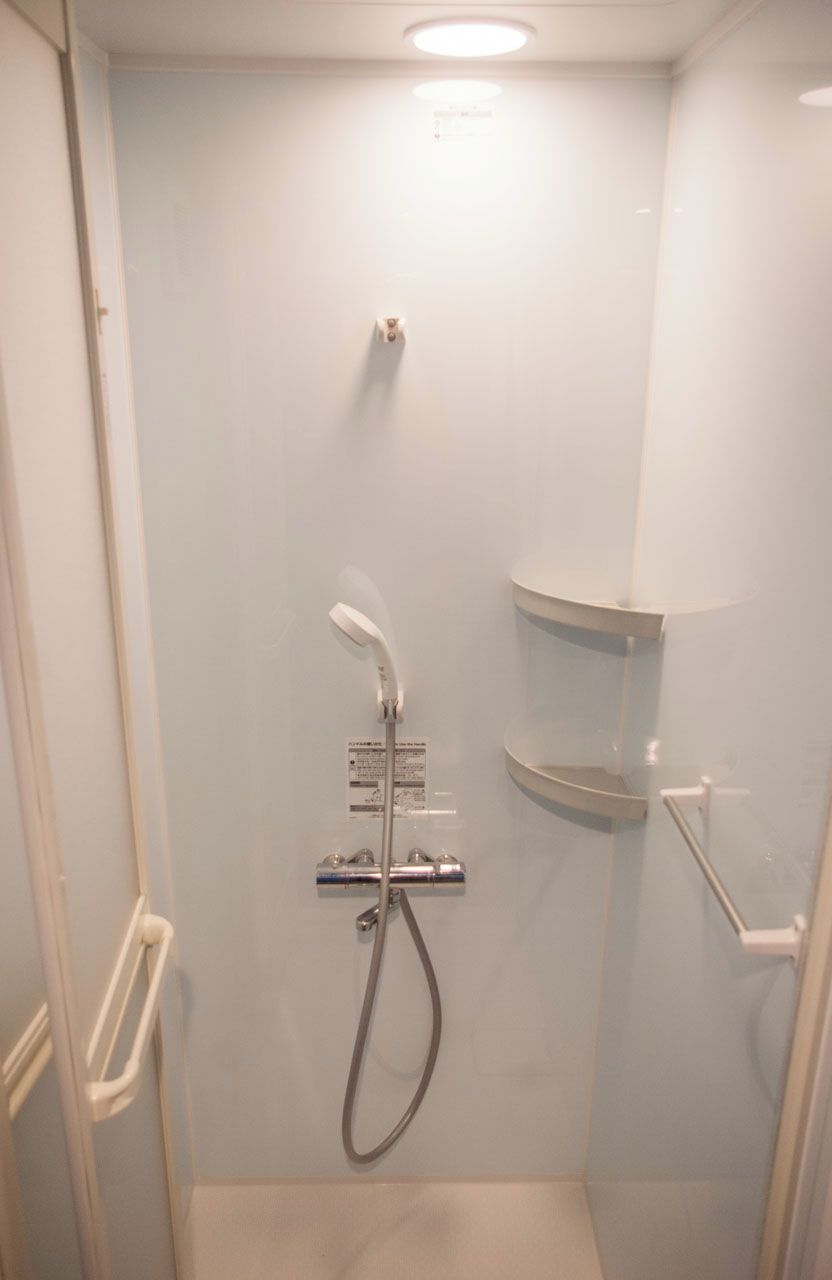 A small, enclosed shower stall with a handheld showerhead and a wall-mounted faucet.