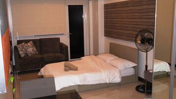A hotel room with a bed, a sofa, a desk, a mirror, and a fan.