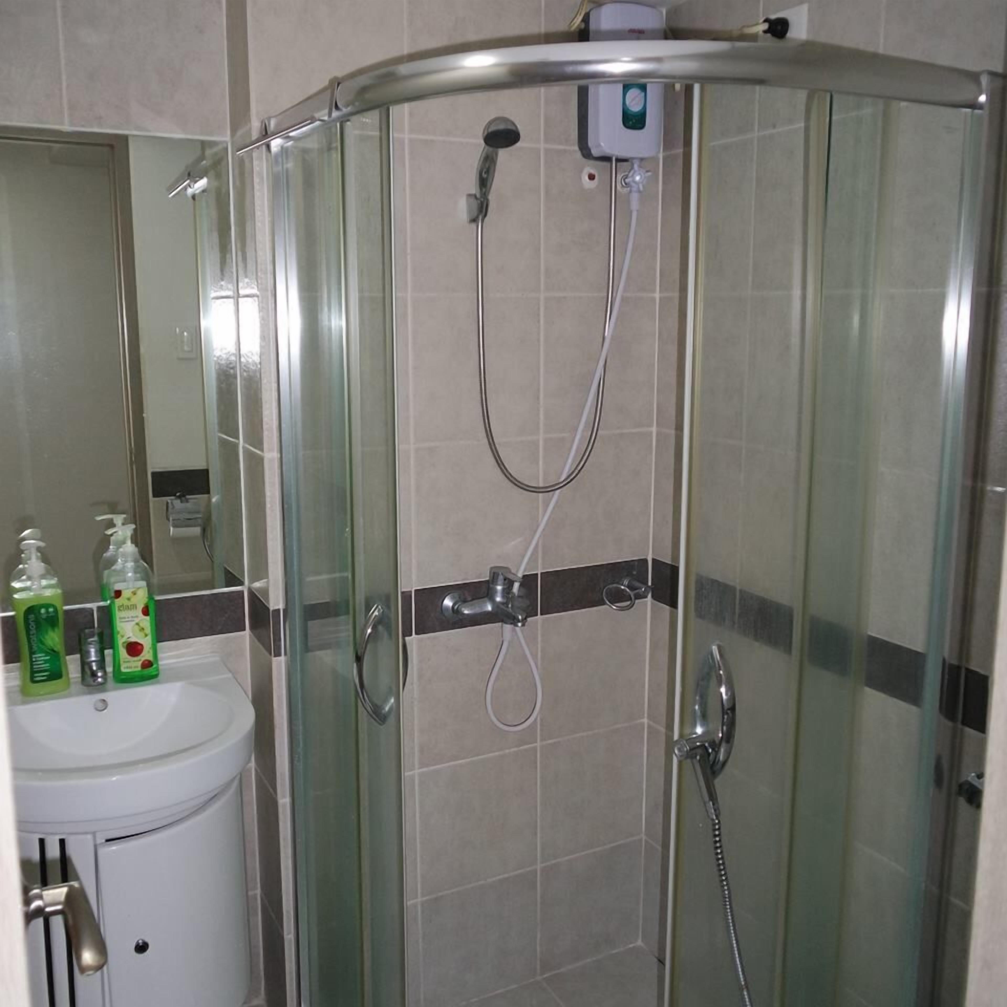 A glass-enclosed shower with a handheld showerhead and a wall-mounted faucet.
