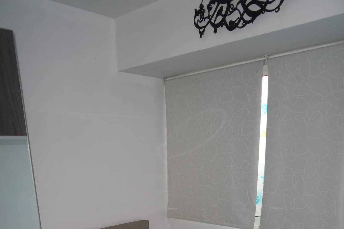 Une chambre à coucher comprenant un lit, une table de chevet, une fenêtre avec des rideaux et un climatiseur fixé au mur.
