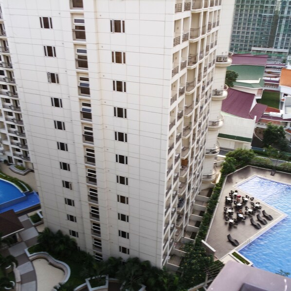 A high-rise building with multiple balconies and a swimming pool area with lounge chairs.