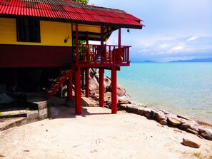 Ein Strandhaus mit rotem Balkon, gelb-roter Fassade und Blick auf den Ozean.