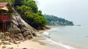 A beach with a wooden structure, large rocks, and houses in the background. - Golden Beach Resort (Ko Pha-ngan)