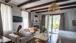 Une pièce chaleureuse avec un canapé, une table en bois, un téléviseur fixé au mur et une grande fenêtre avec des rideaux.