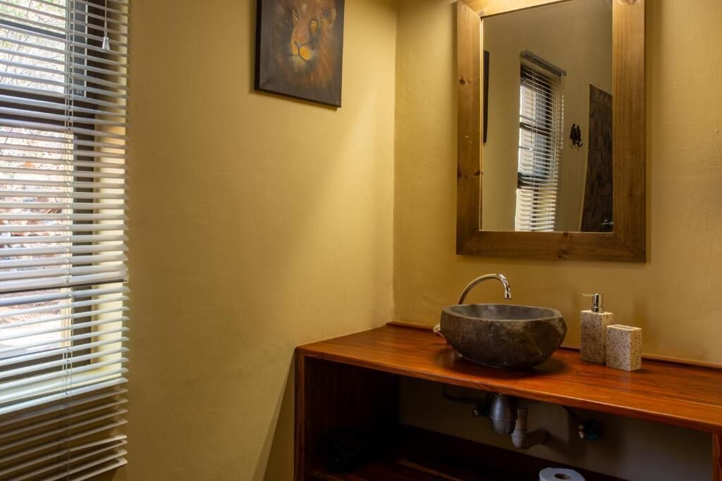 A bathroom with a wooden vanity, a stone sink, a mirror, and a window with blinds.