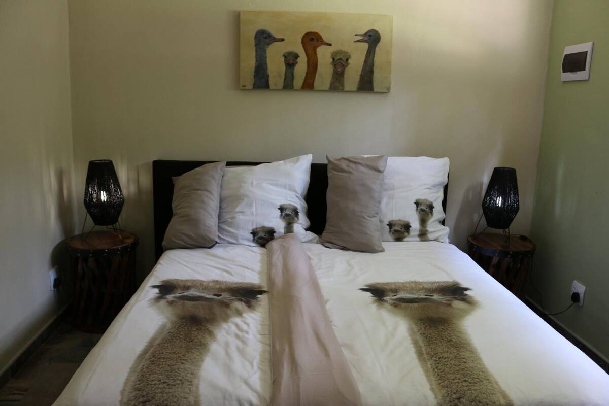 Un lit au design original, orné d’imprimés d’autruches, avec un tableau représentant des autruches accroché au mur, et deux lampes placées de part et d’autre.