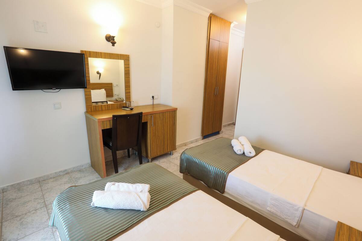 A hotel room with two single beds, a desk with a chair, a television mounted on the wall, and a wardrobe.