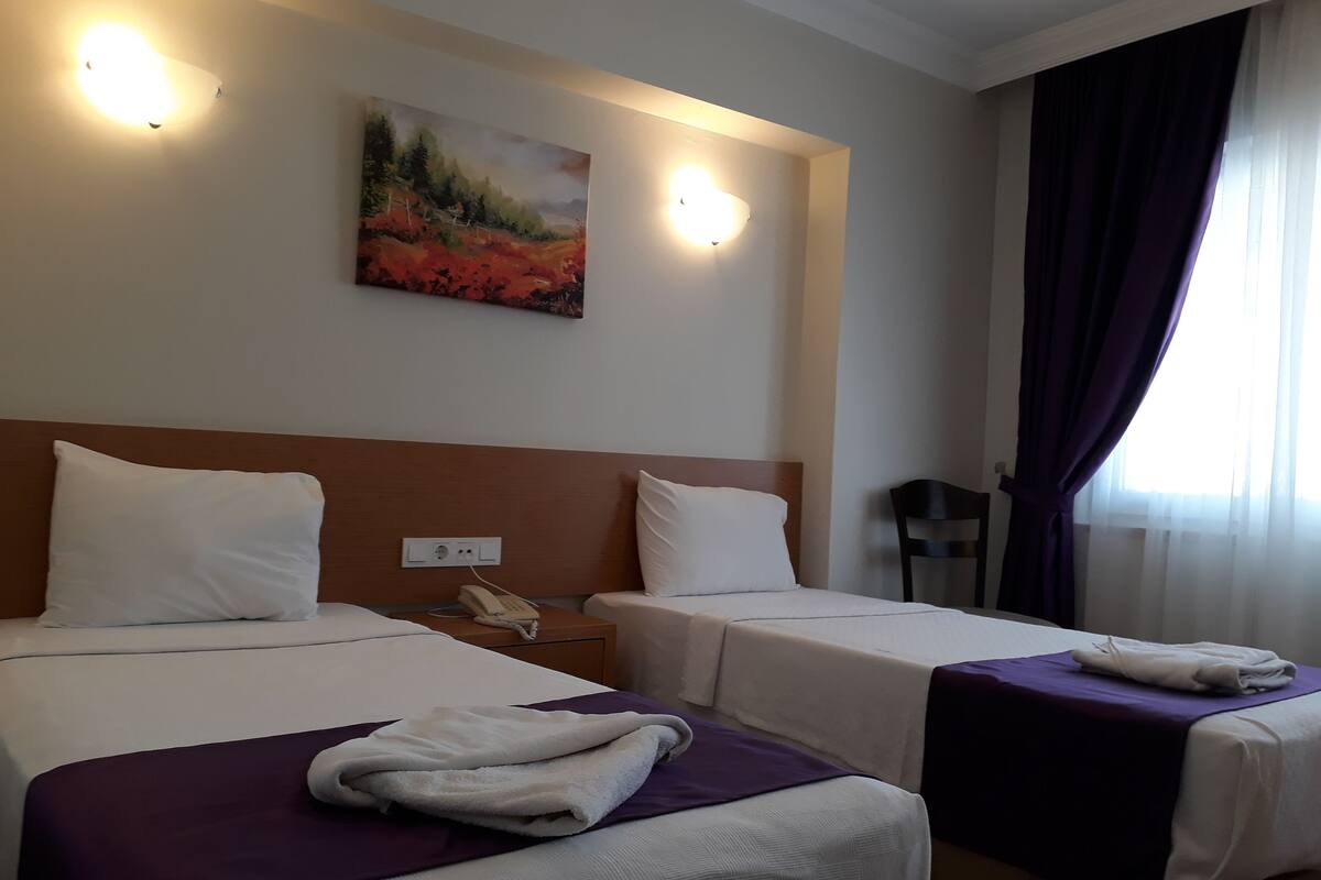A hotel room with two beds, a painting on the wall, and a window with curtains.