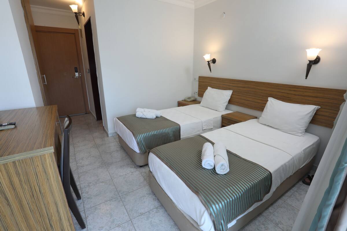 A hotel room with two beds, a wooden desk, and a door.