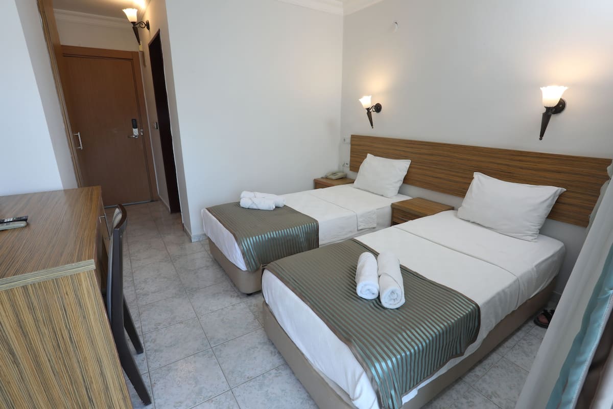 A hotel room with two beds, a wooden desk, and a door.