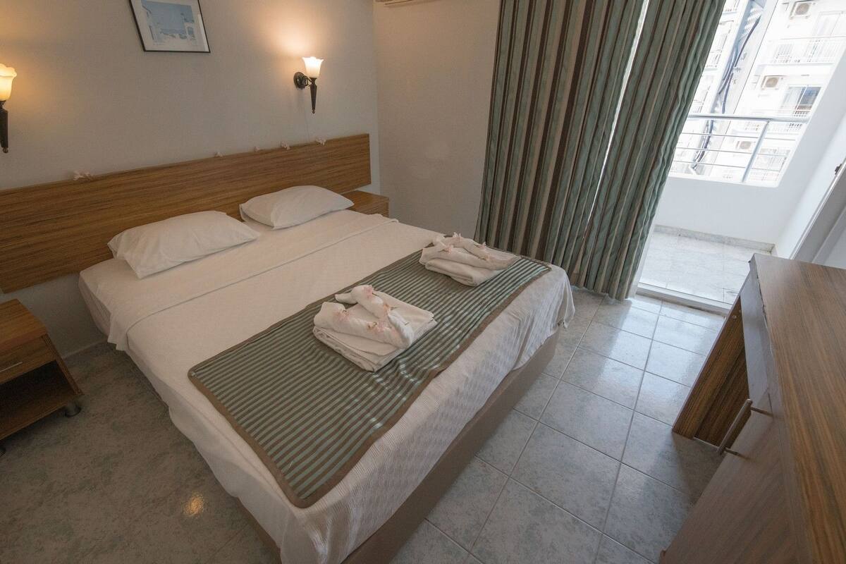 A hotel room with a large bed, two bedside tables, a telephone, and a window with curtains.