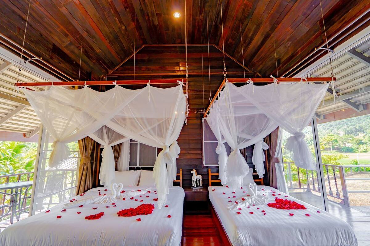 A room with two beds, each with a canopy, and a balcony with a railing.