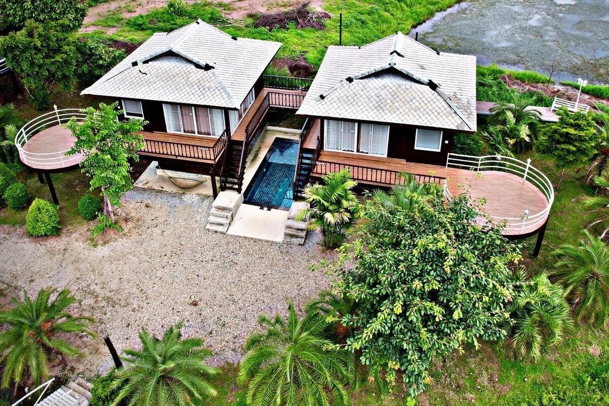 A bungalow with a swimming pool, surrounded by lush greenery and palm trees.