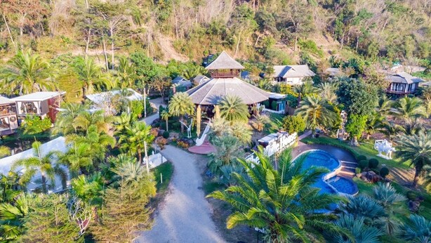 An aerial view of a resort with multiple buildings, a central structure with a thatched roof, and a swimming pool surrounded by palm trees. - The White House Boutique Chiangrai (Chiang Rai)