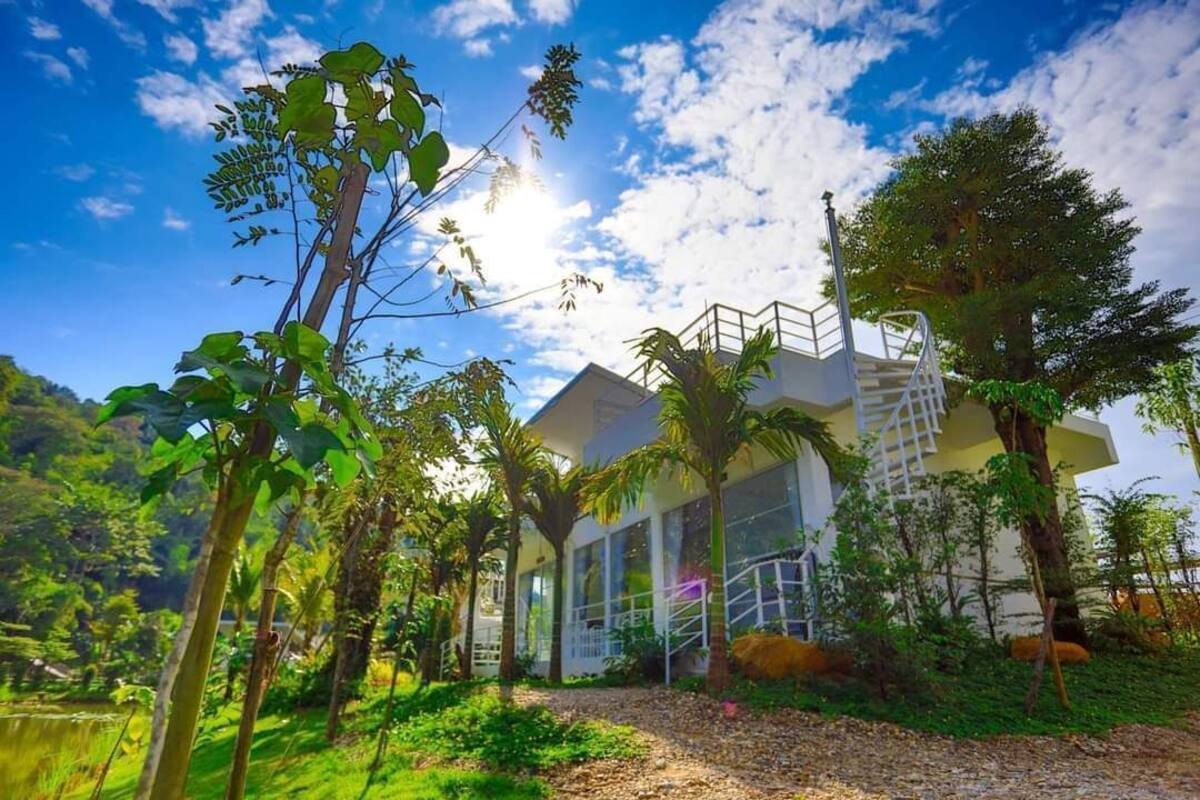 A modern building with a glass facade, surrounded by lush greenery and a clear blue sky.