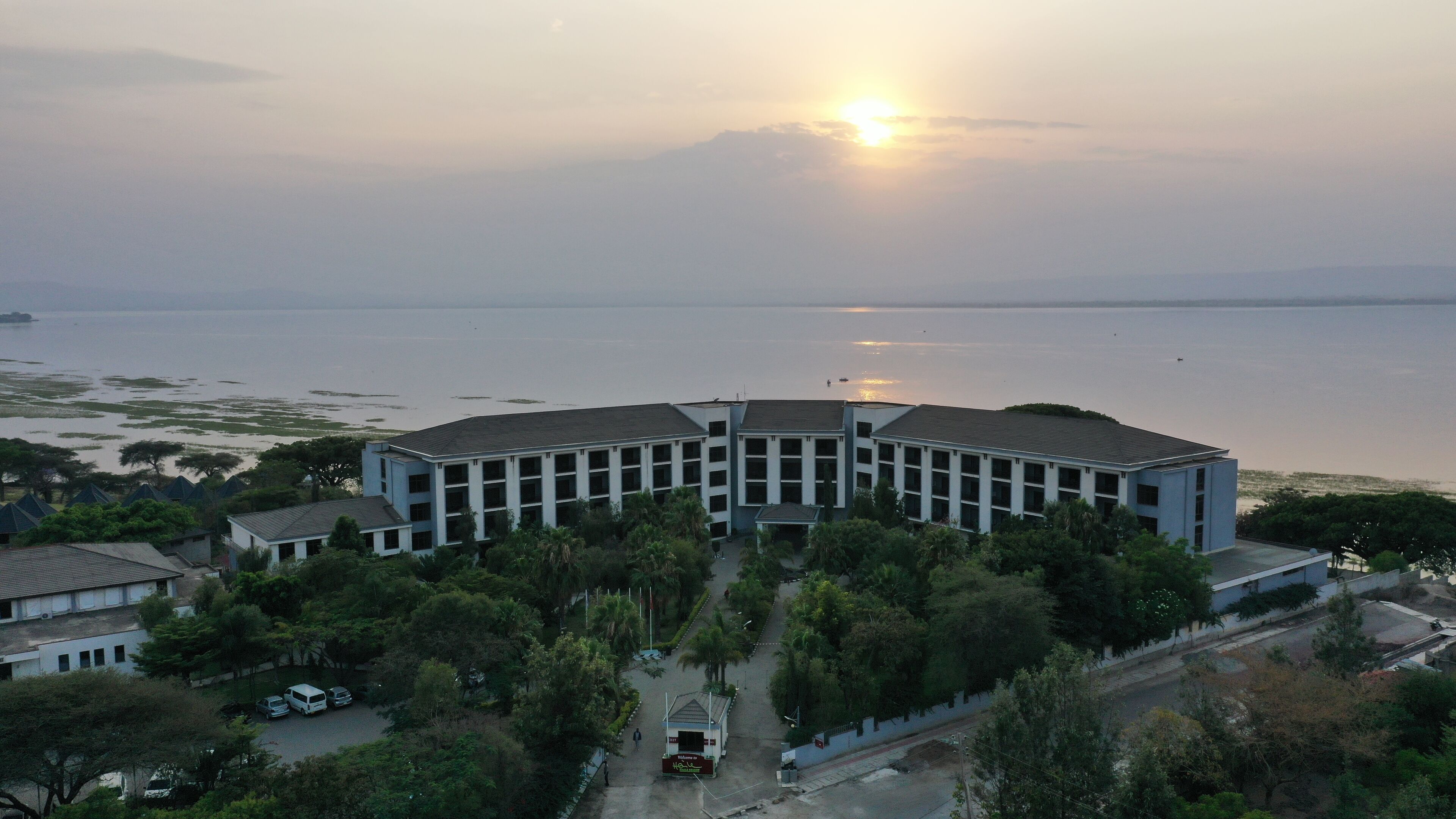 A large, modern building with a circular layout, surrounded by lush greenery and a body of water.