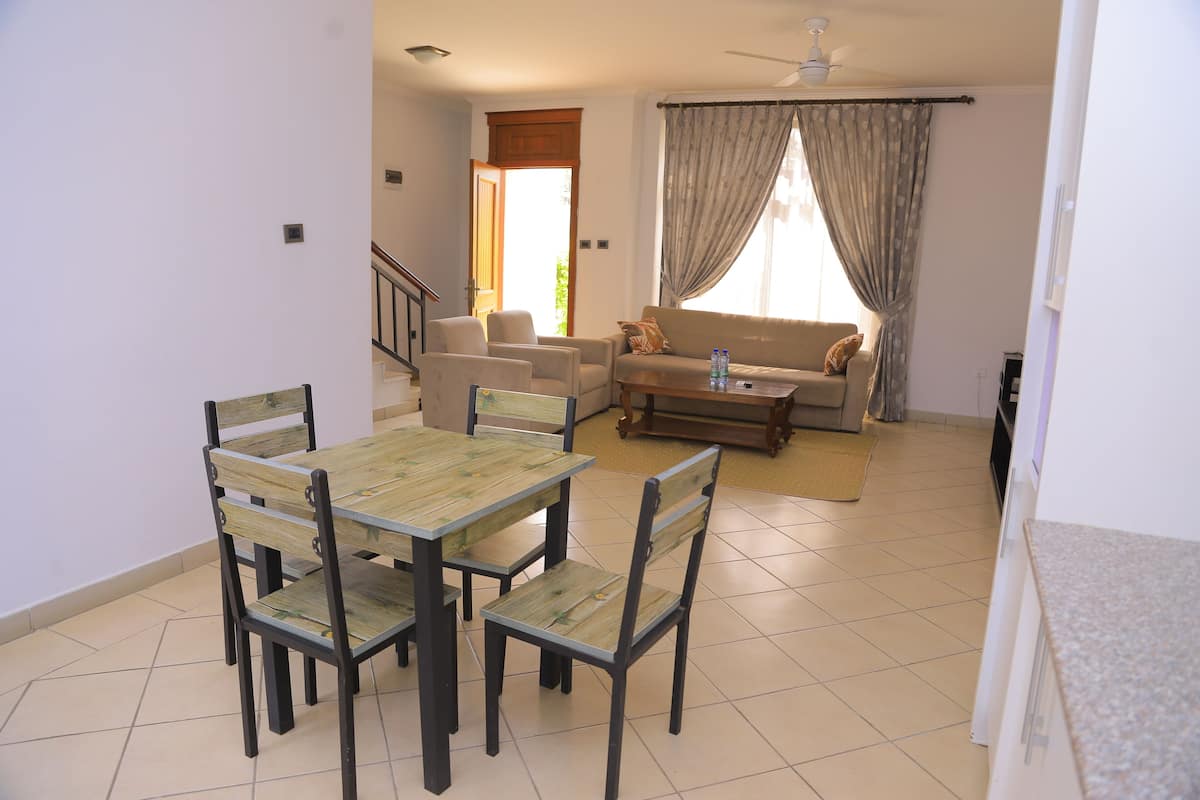 A dining area with a wooden table and chairs, a sofa, and a window with curtains.