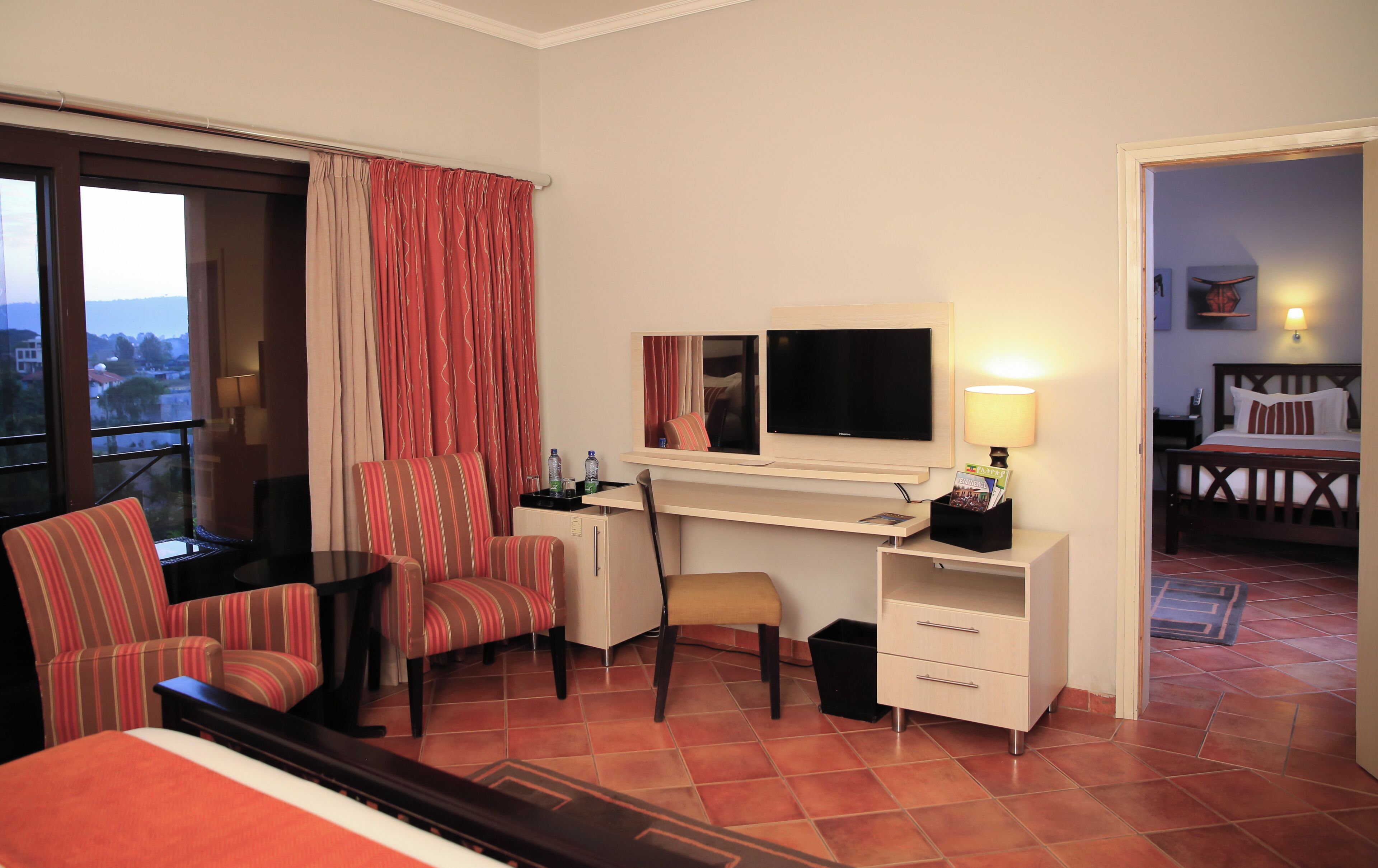 Habitación de hotel con cama, escritorio con computadora, silla, televisor y ventana con cortinas.