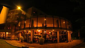 A modern hotel with a circular glass facade, outdoor seating area, and a staircase leading to the upper floors.