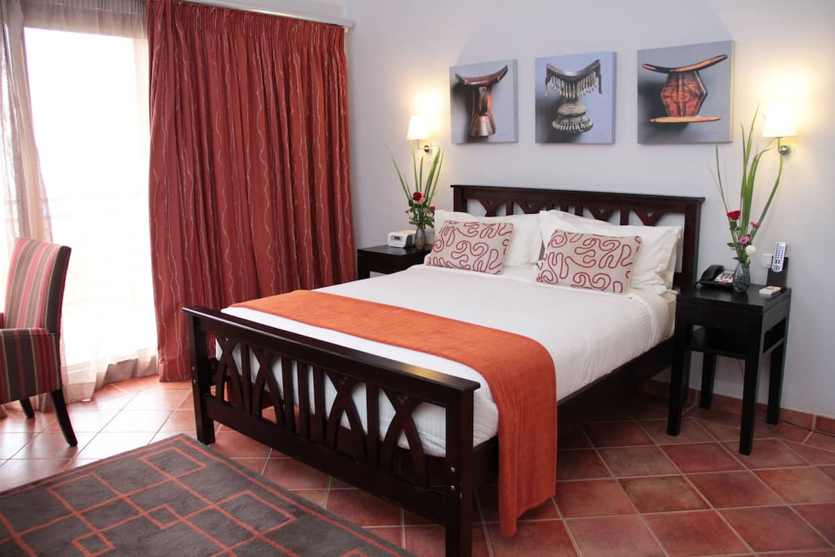 A bedroom with a wooden bed, a nightstand, a chair, a window with curtains, and wall art.