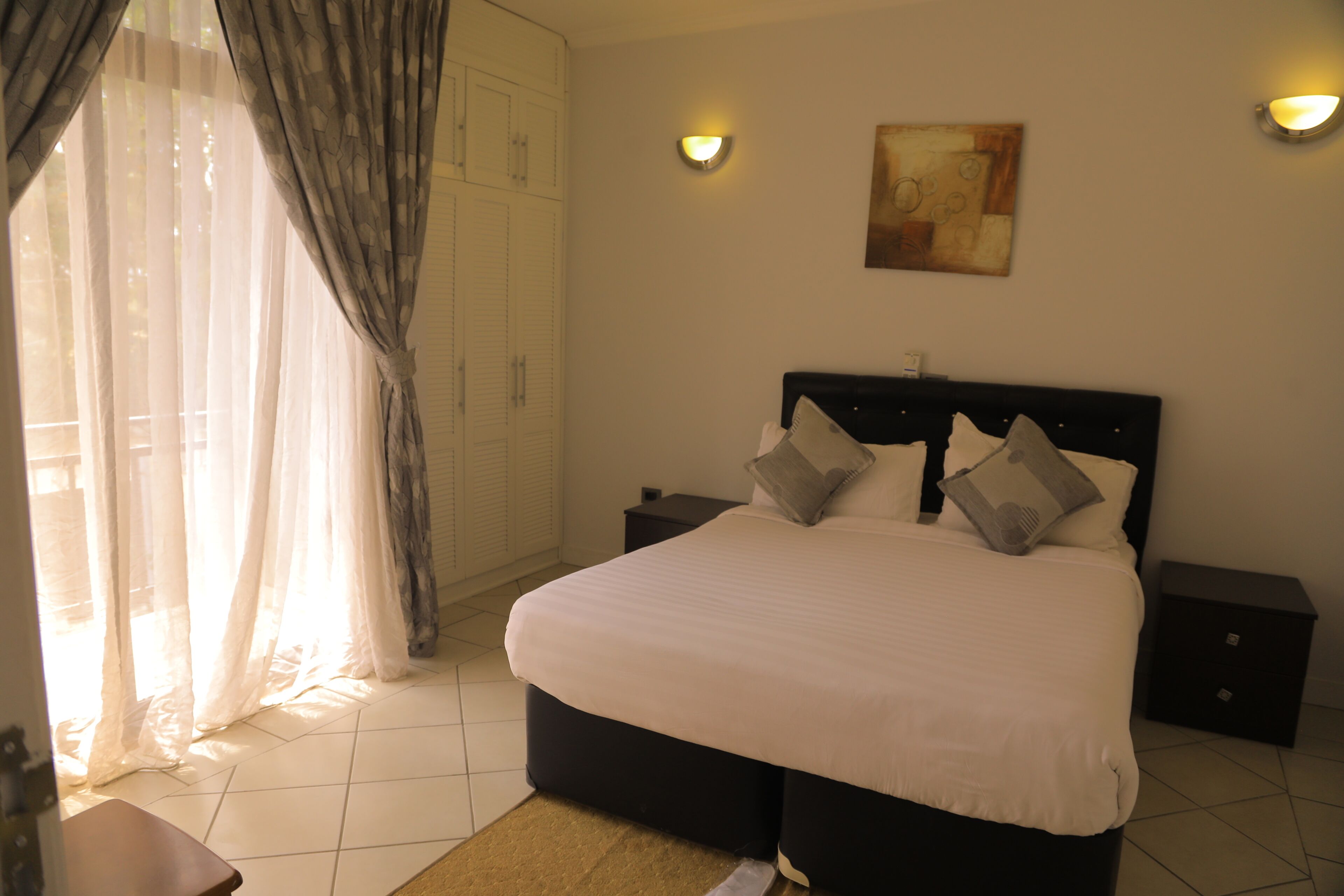 Un dormitorio con cama, mesitas de noche, una lámpara de pared y un cuadro.