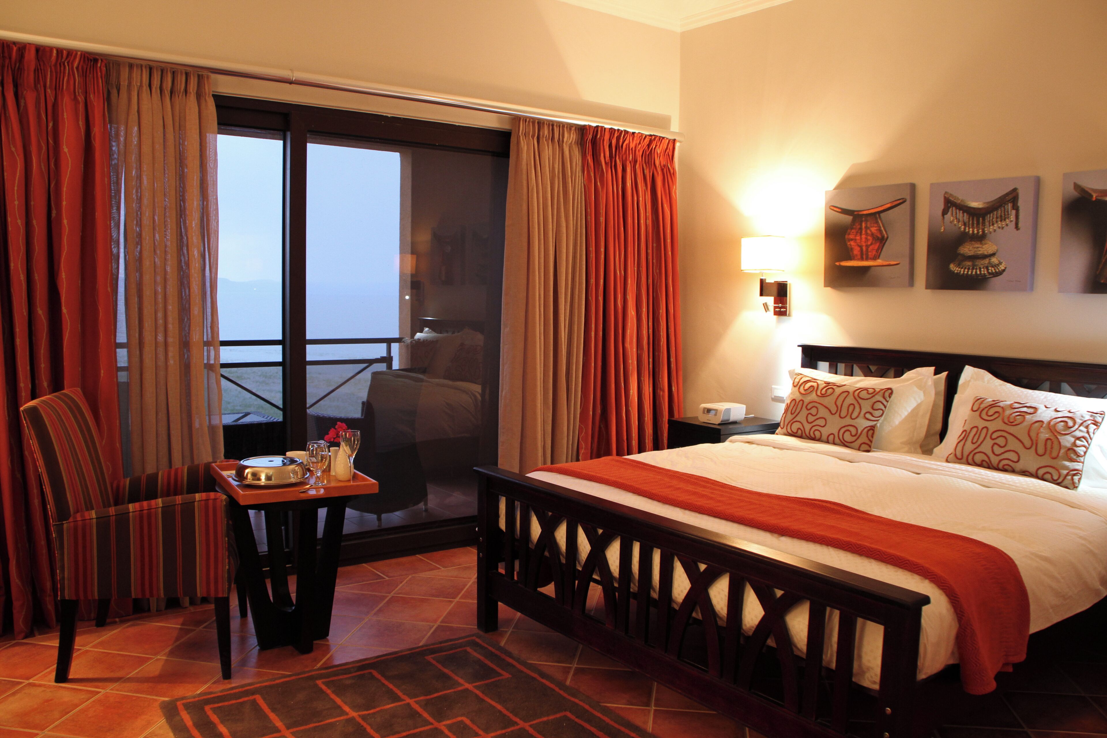 Habitación de hotel con cama, una silla, una mesa con bandeja y un balcón con asiento.