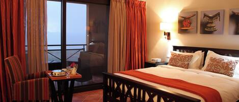 Habitación de hotel con cama, una silla, una mesa con bandeja y un balcón con asiento.
