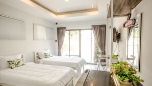 Habitación de hotel con dos camas, una mesa de madera, una planta en maceta y un televisor montado en la pared.