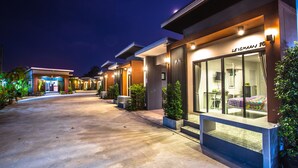 Un hotel moderno con una entrada bien iluminada, asientos al aire libre y una habitación visible con cama.