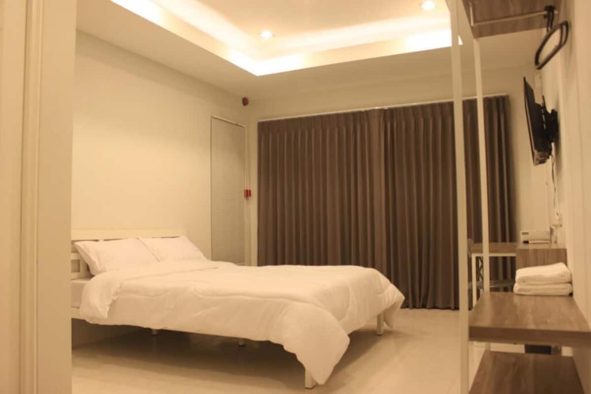 A bedroom with a bed, a bedside table, a mirror, and a window with curtains.
