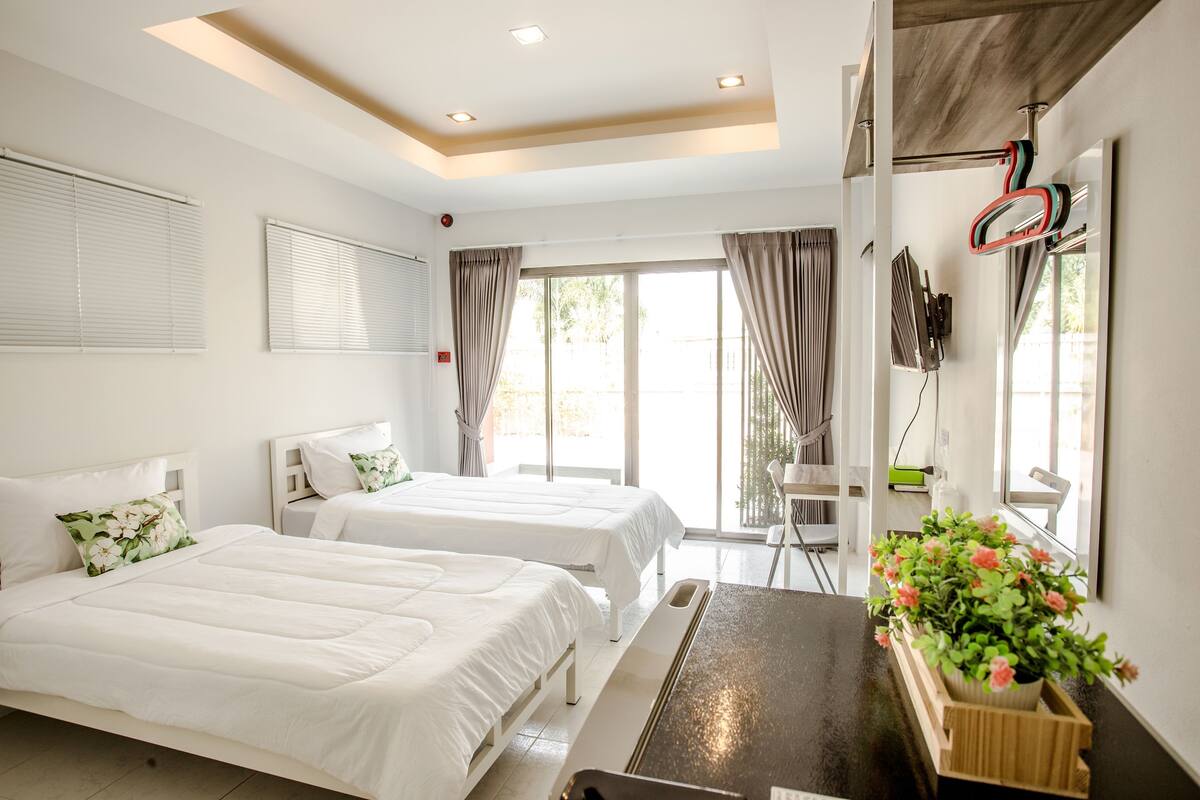 A hotel room with two beds, a desk, a chair, a TV, and a window with curtains.