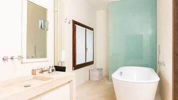 Un baño moderno con una bañera independiente, un espejo grande y un tocador con lavamanos y toallero.