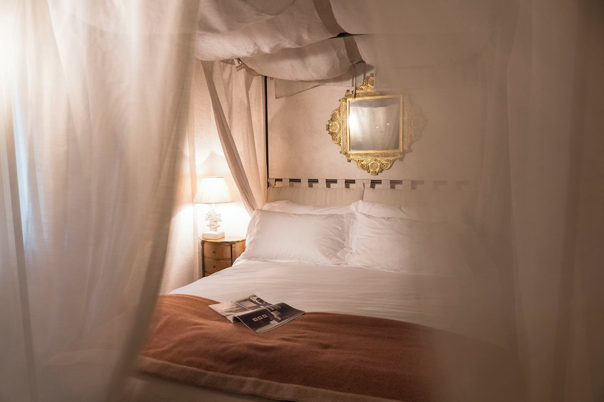 A bed with a canopy, a bedside table with a lamp, and a mirror on the wall.