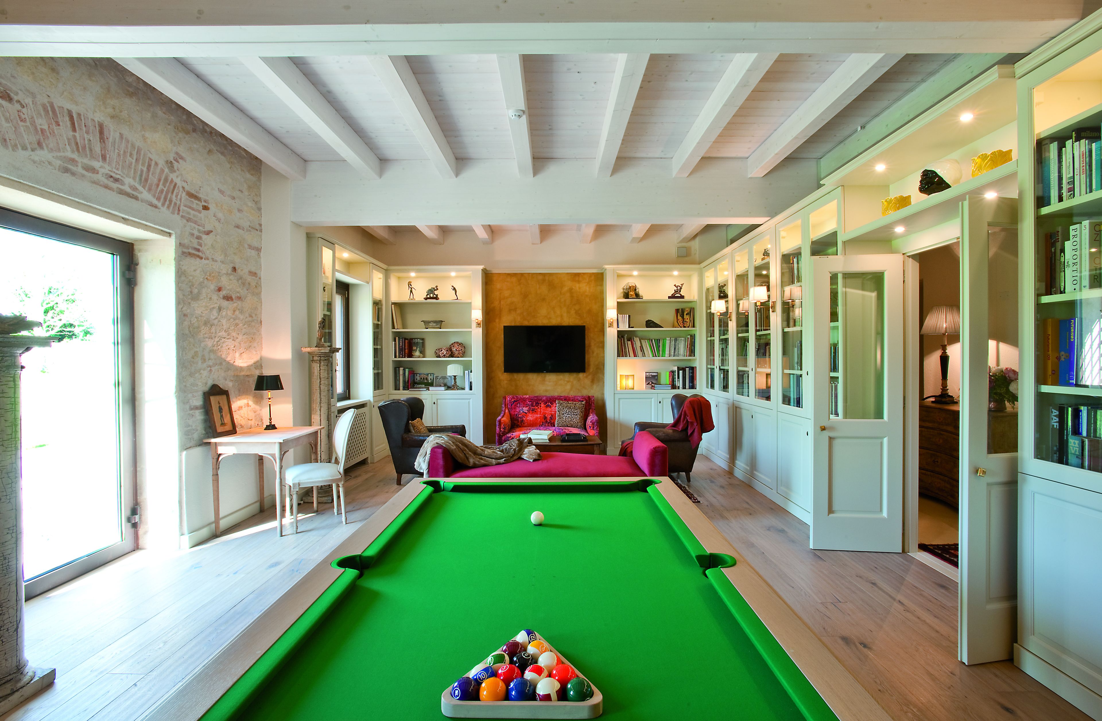 Una mesa de billar en una habitación con pared de ladrillo, un sofá y estanterías.